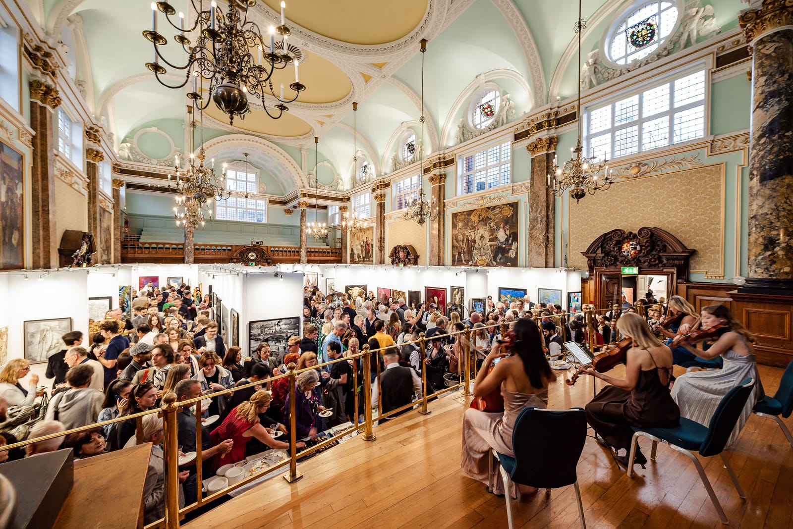 A string quartet playing on the balcony above the crowded main hall during a private view.