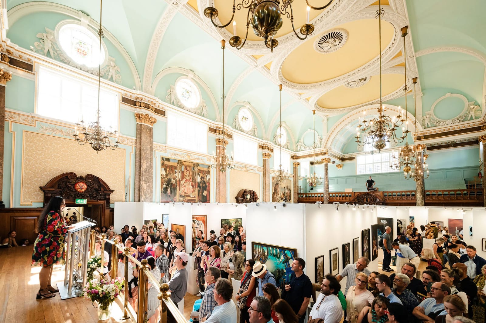 The awards ceremony seen from the balcony: a crowd filling the main hall beneath gilded plasterwork and chandeliers.