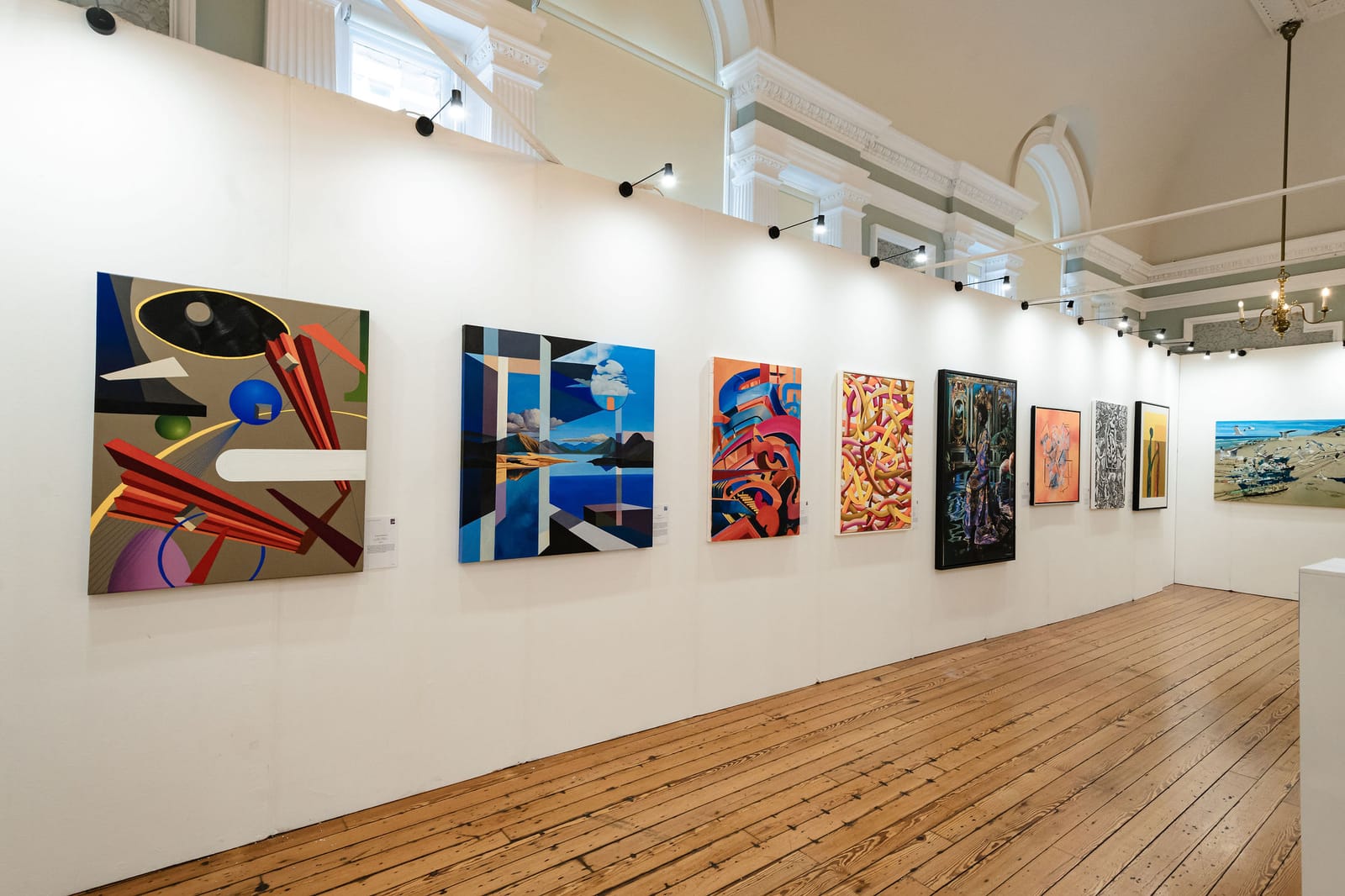 A long white gallery wall inside the Biennale, hung with a run of contemporary paintings that recedes away over a bare wooden floor.