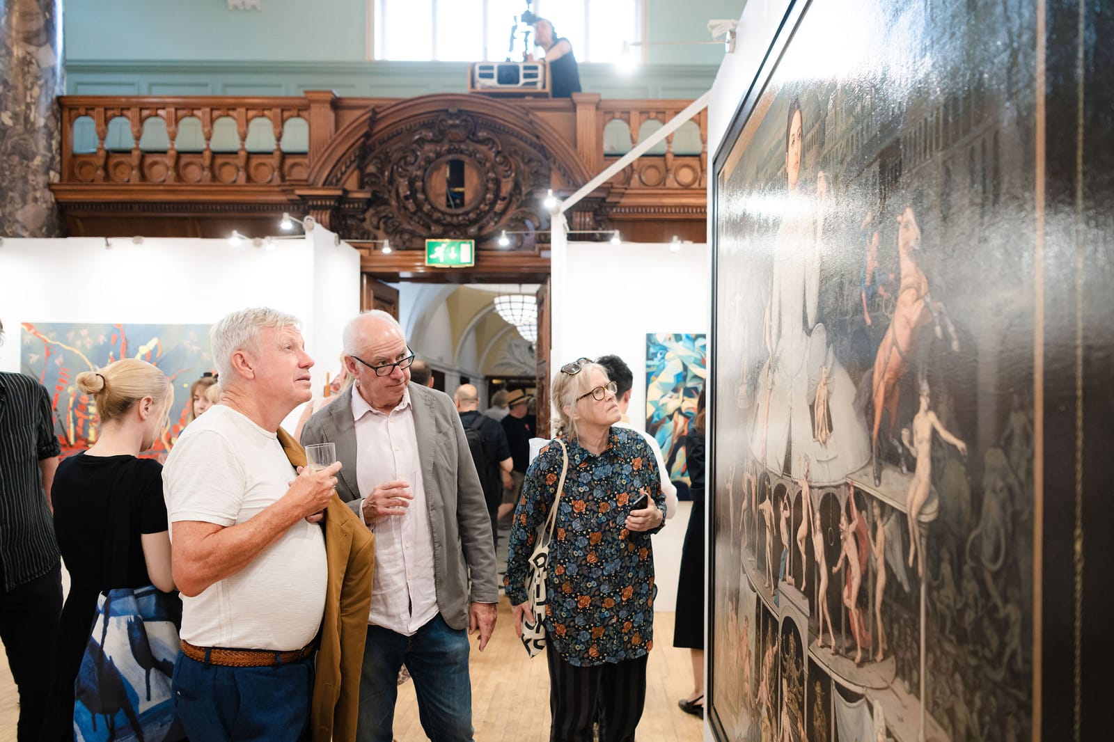 Visitors in conversation beneath the painted and gilded ceiling of the main hall at the private view.