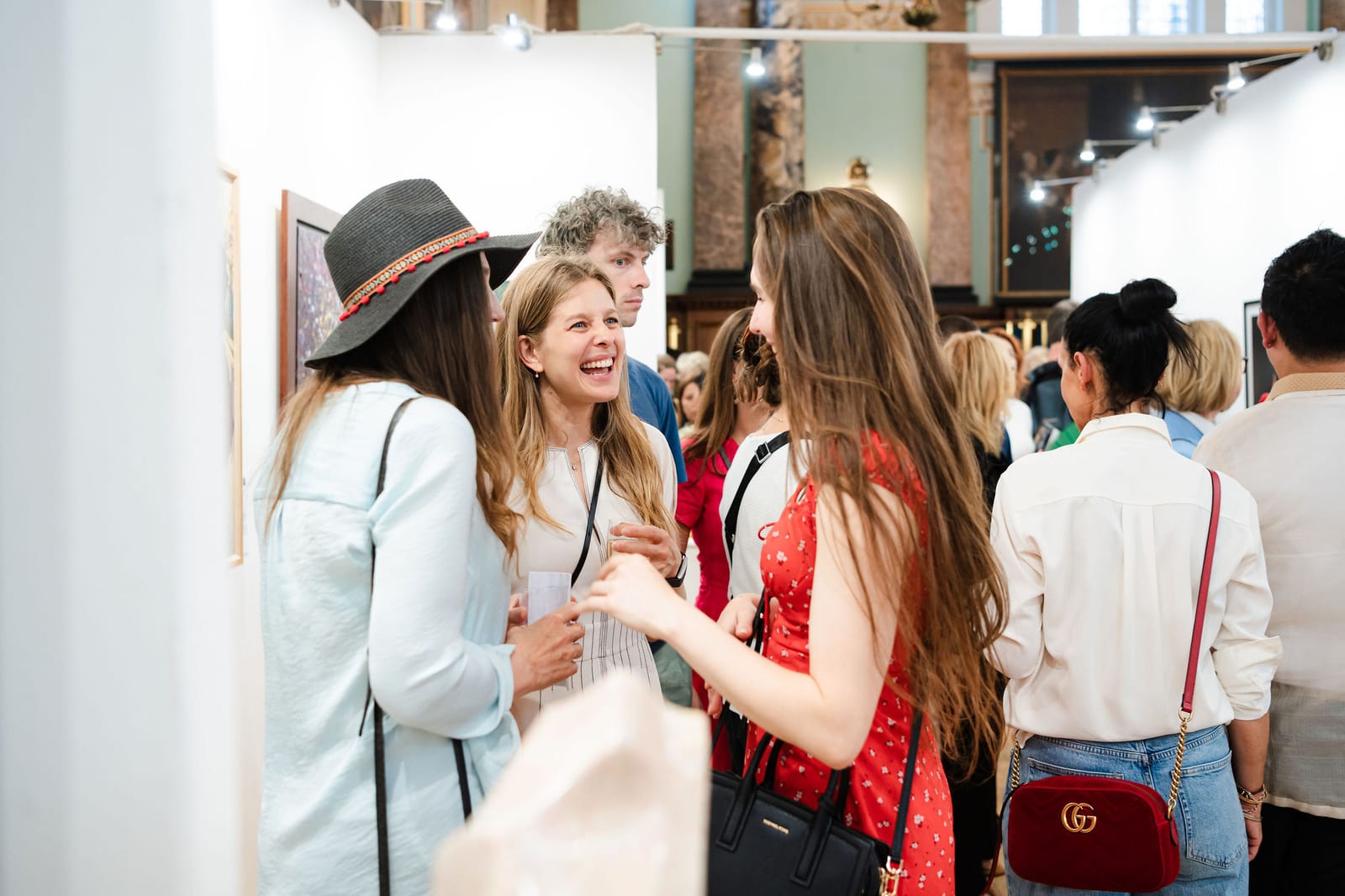 Guests laughing together at the private view, the crowd stretching back between the exhibition walls.