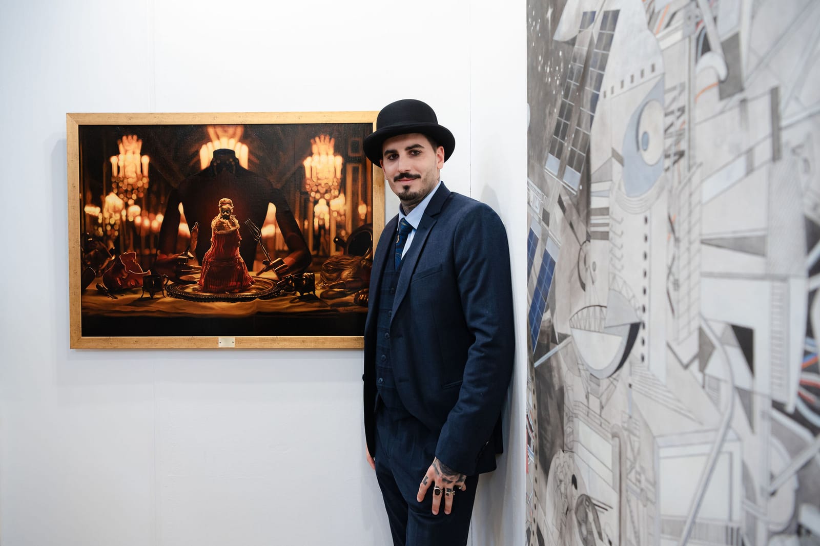 A visitor in a bowler hat standing between two hung works, one a gilt-framed painting.